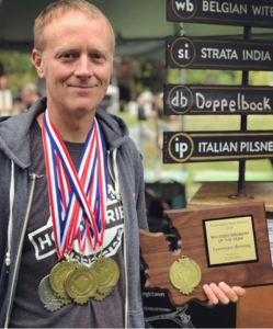 John, head brewer and co-owner owner of Lowercase Brewing with medals around his neck from the Great American Beer Festival